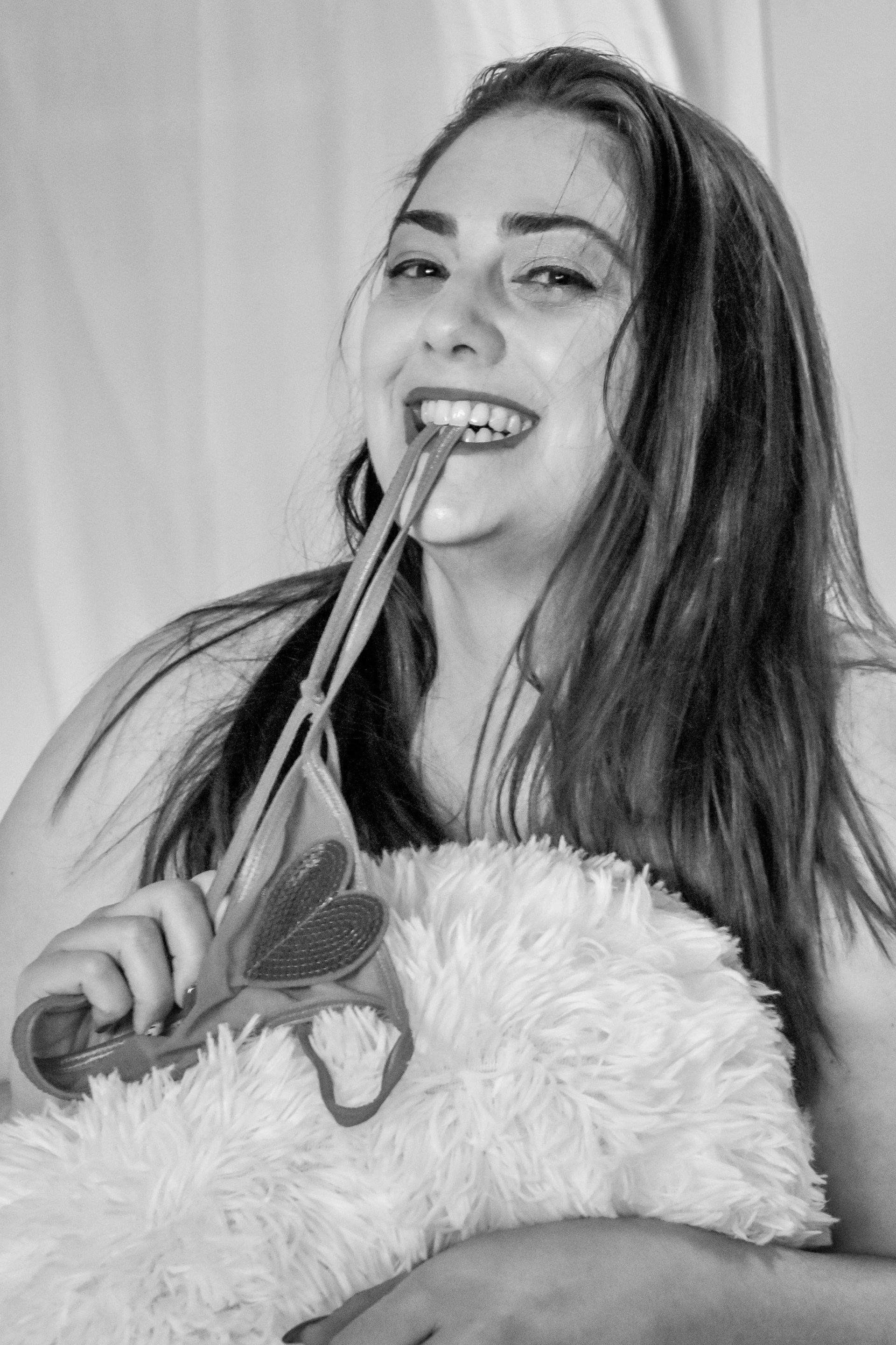 A black and white photo of a woman holding a rose in her mouth.