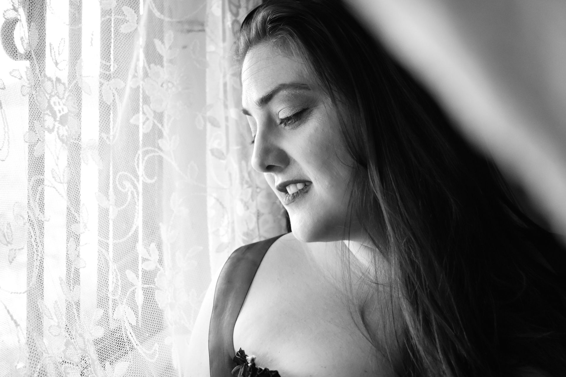 A black and white photo of a woman in lingerie looking out a window.