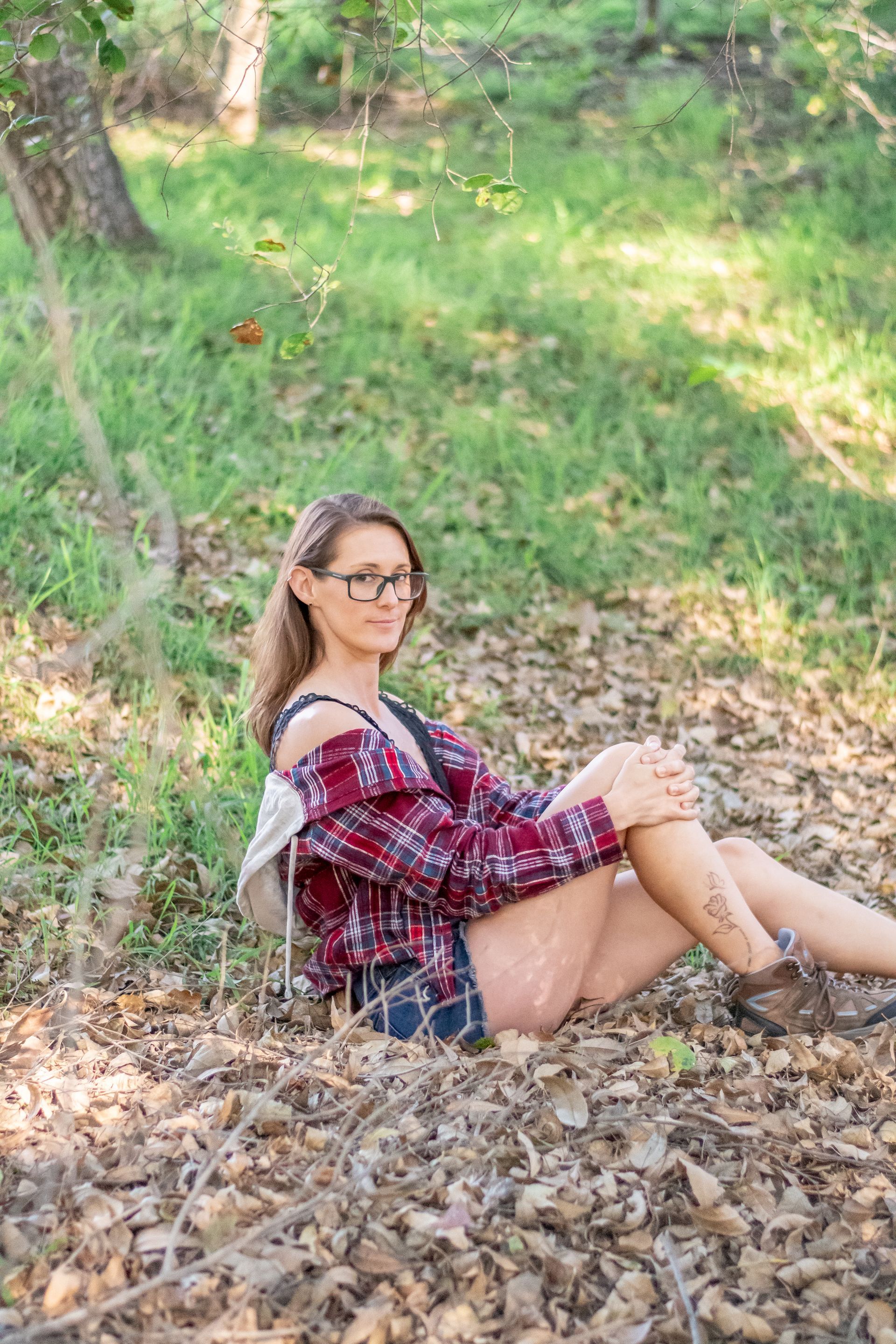 A woman is sitting on the ground in the woods with a backpack.