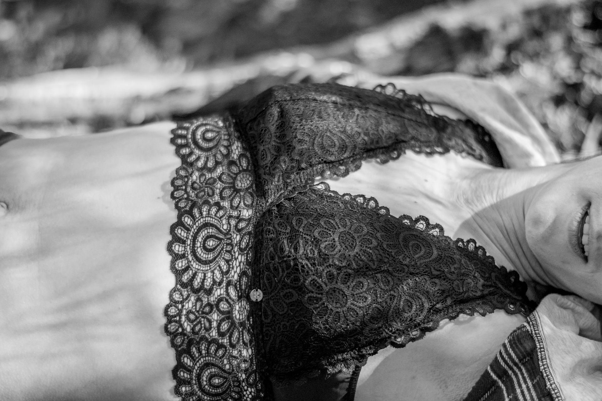 A black and white photo of a woman laying on her stomach wearing a black lace bra.