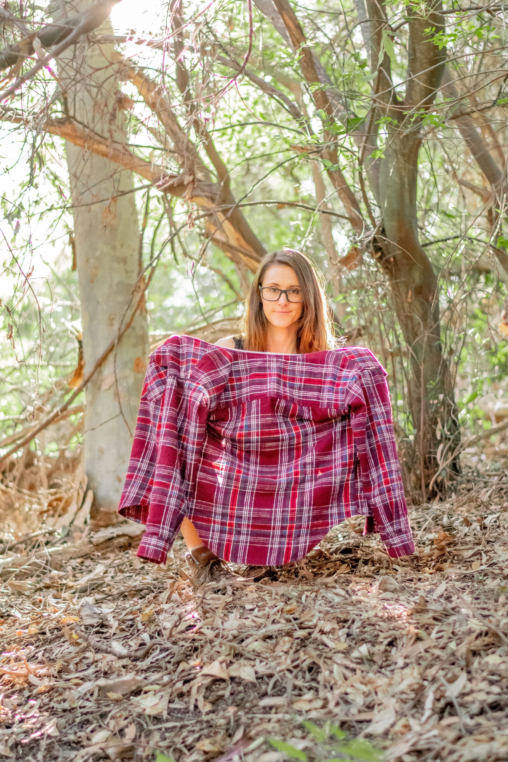 A woman is sitting in the woods holding a plaid shirt.