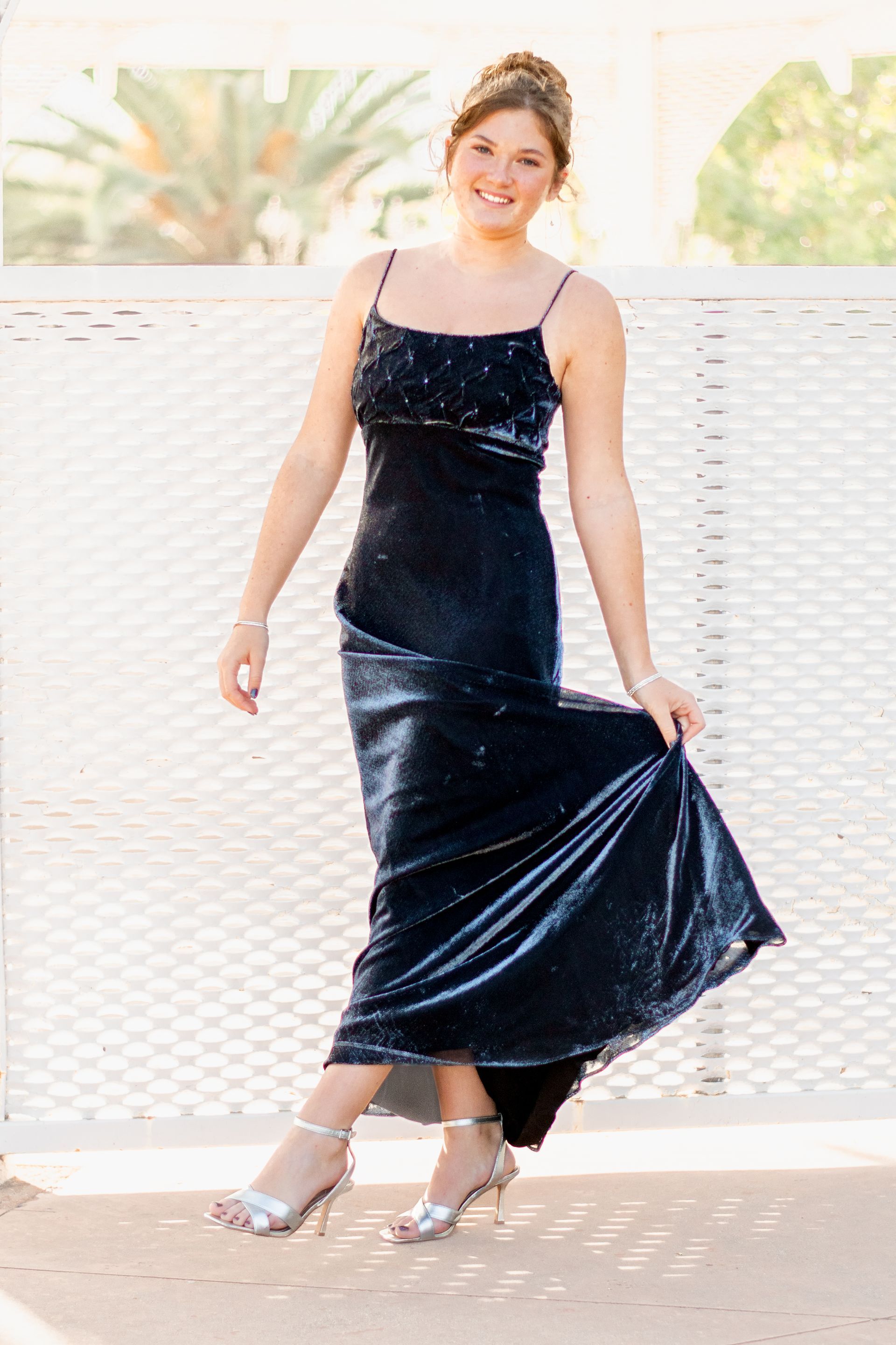 A woman in a long black dress is standing in front of a white fence in San Pedro, CA