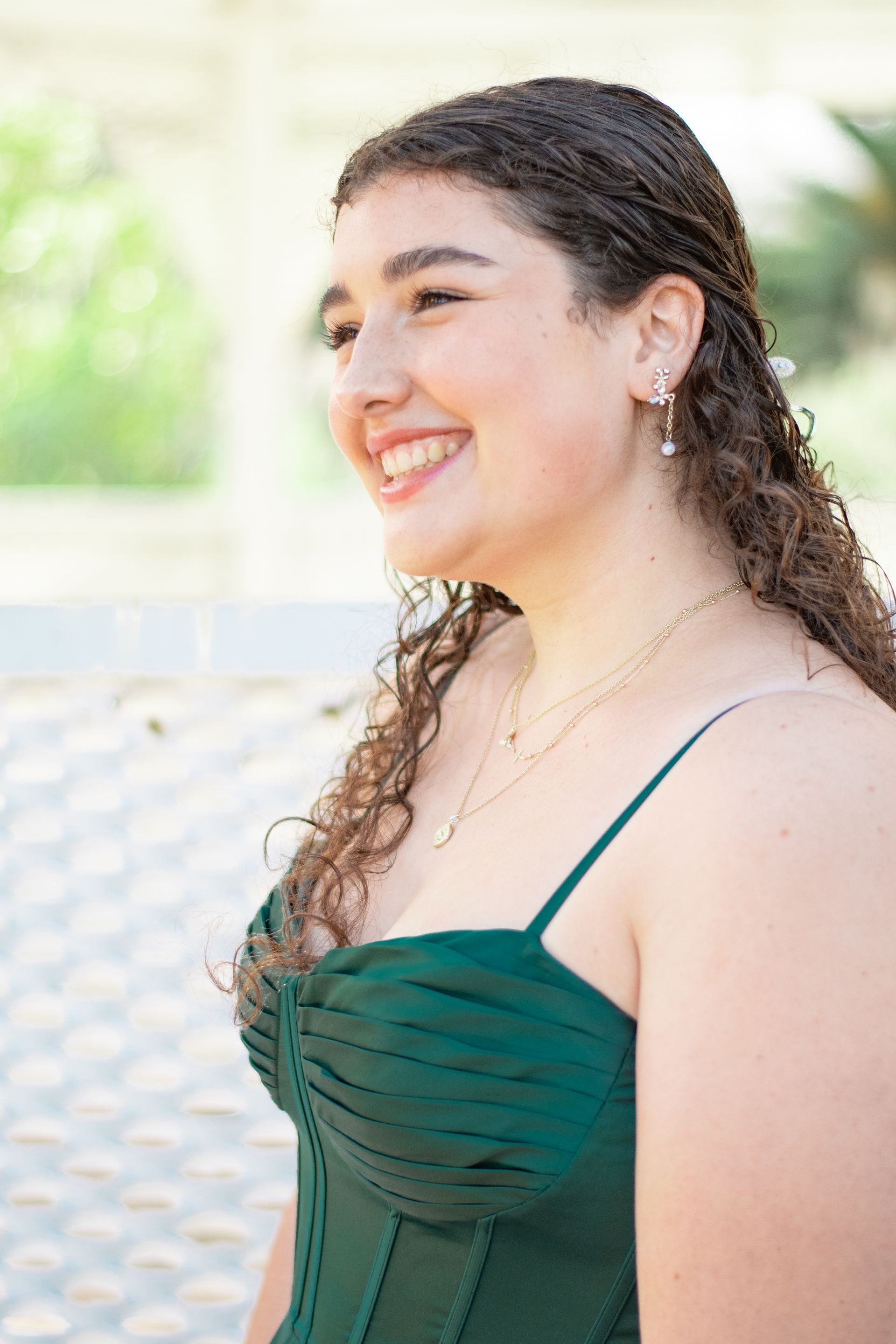 Woman with curly hair in green dress smiles, looking off-camera, outdoors.
