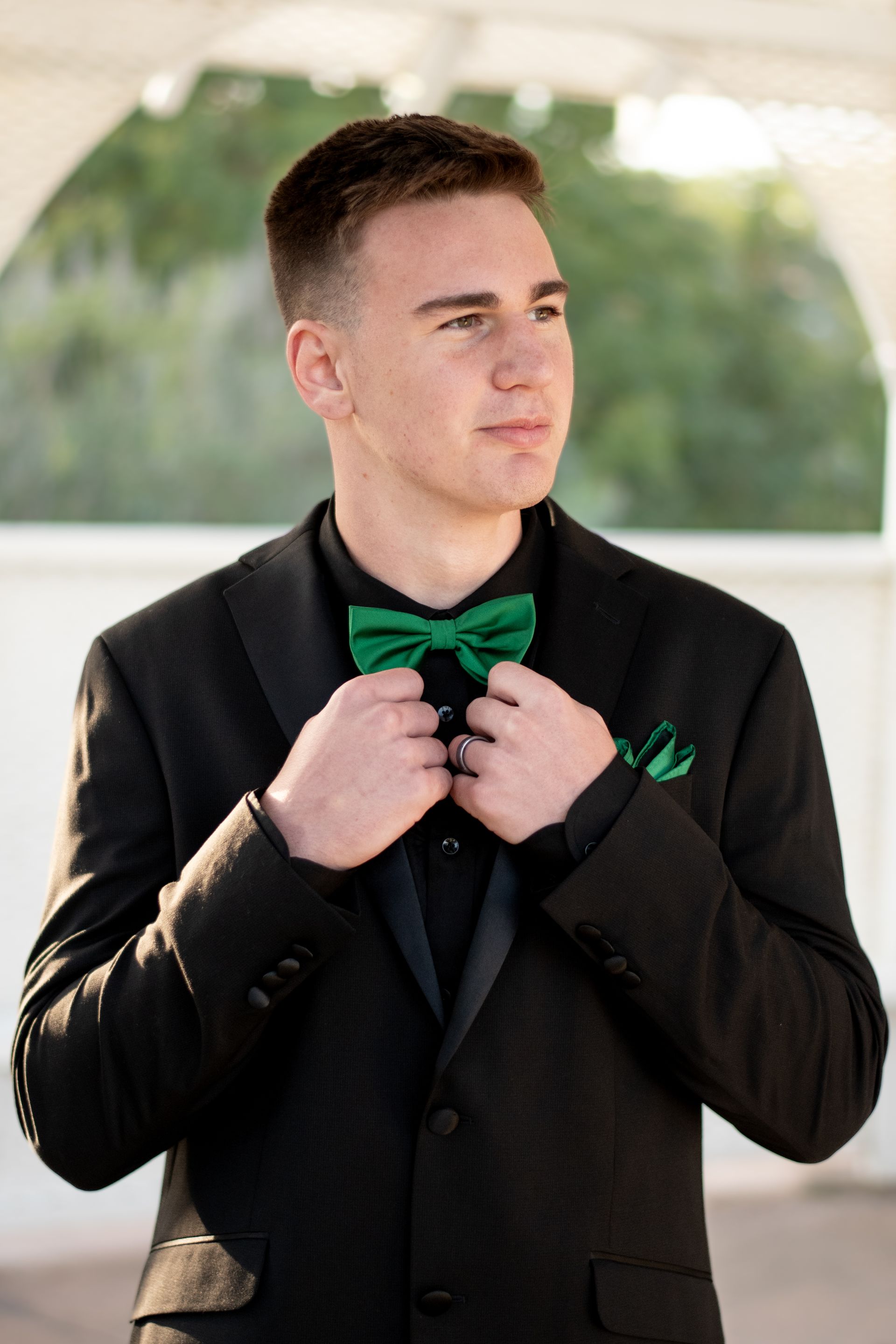 A young man in a black suit and green bow tie is adjusting his bow tie at Averill Park