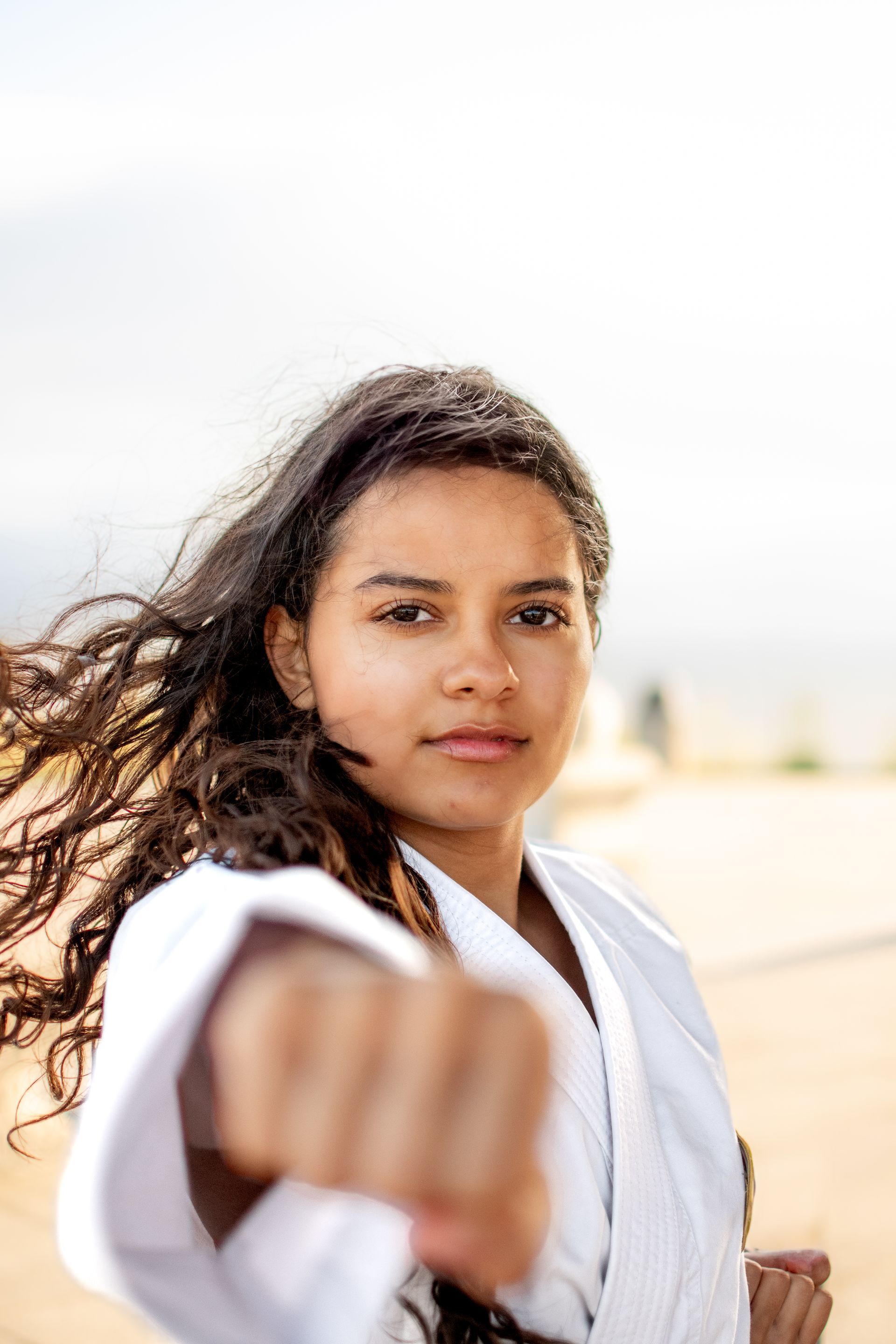 A young girl in a karate uniform is making a fist in the air.