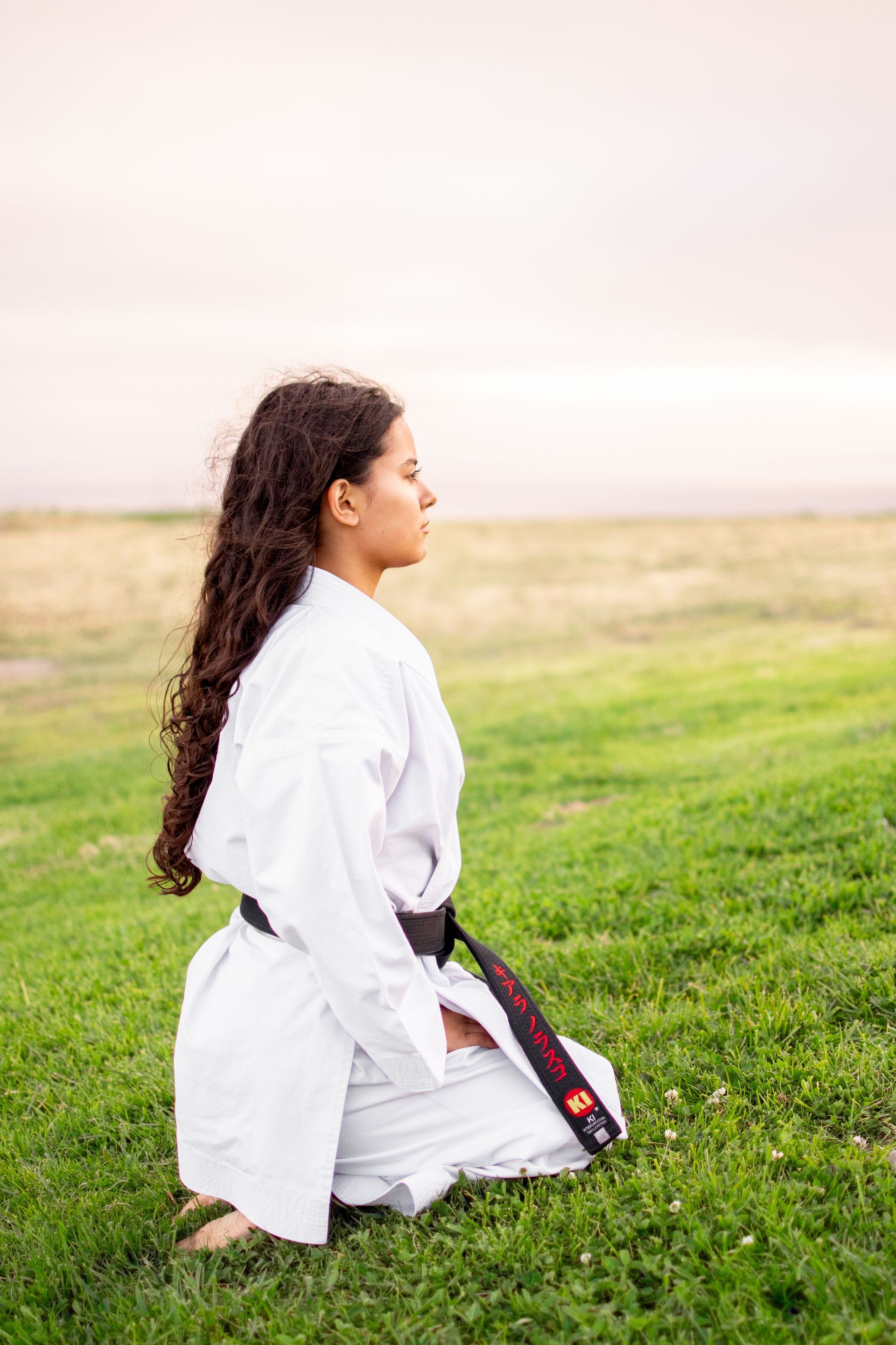 A woman in a karate uniform is kneeling in the grass at Joan Milke Flores Park