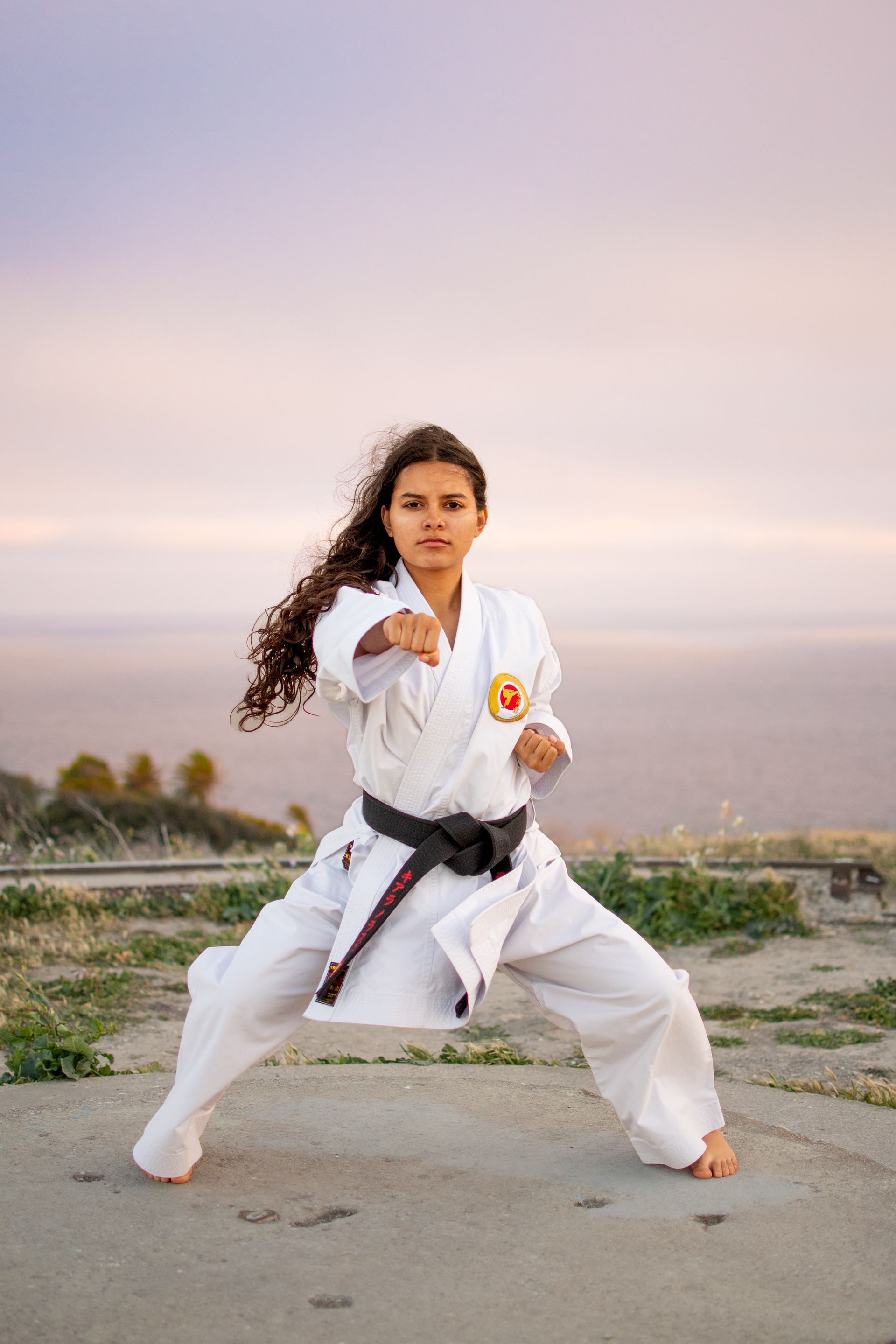 A woman in a karate uniform is practicing karate on a concrete surface by the friendship bell in San Pedro