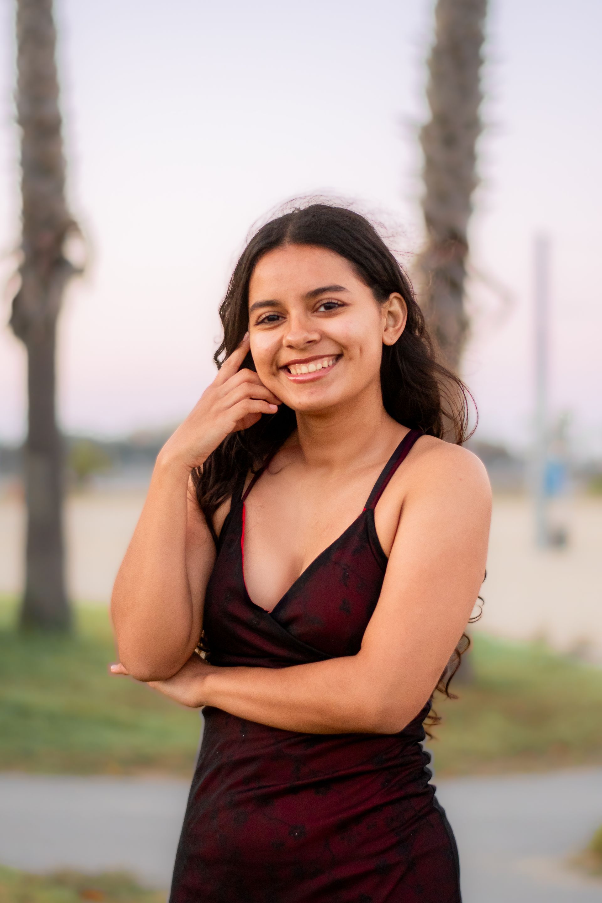 A woman in a red dress is standing with her arms crossed and smiling at Cabrillo Beach