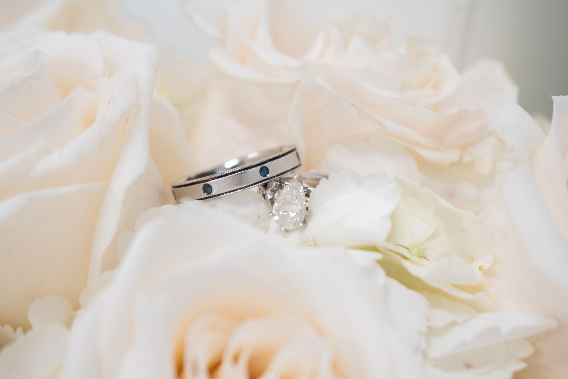 The wedding rings are sitting on top of a bouquet of white roses.