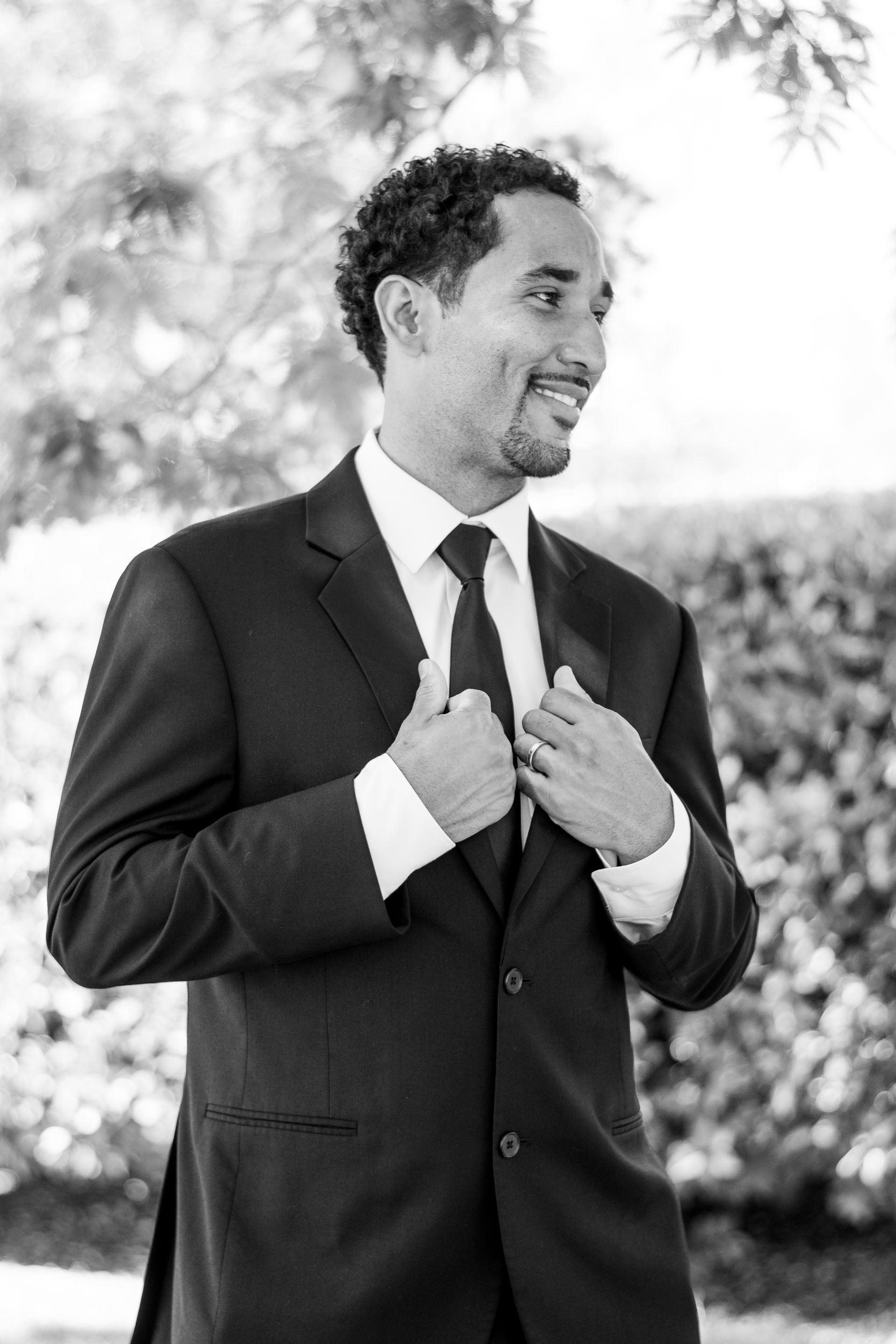 A man in a suit and tie is adjusting his tie in a black and white photo in Lake Forest, CA