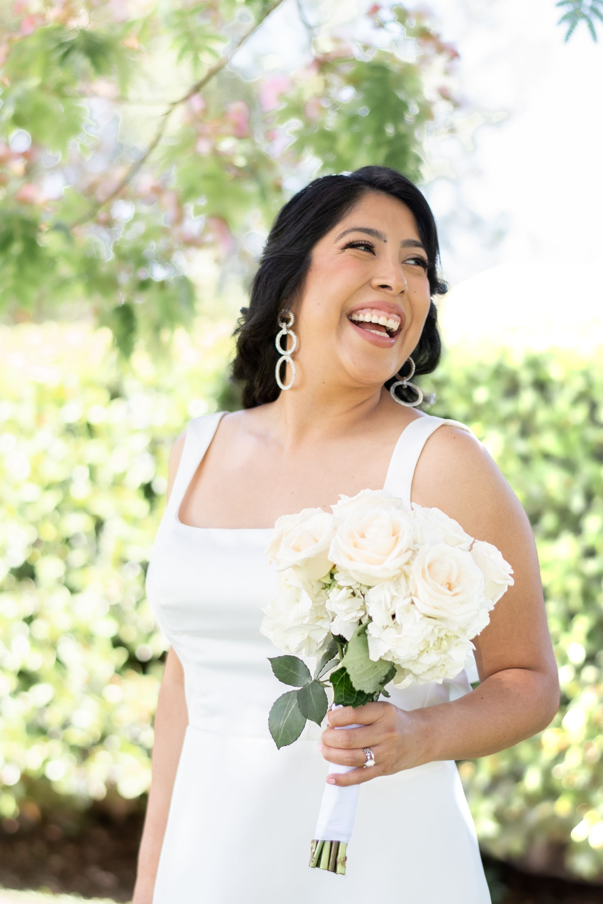 A woman in a white dress is holding a bouquet of white flowers and smiling at Veterans Park in Lake Forest