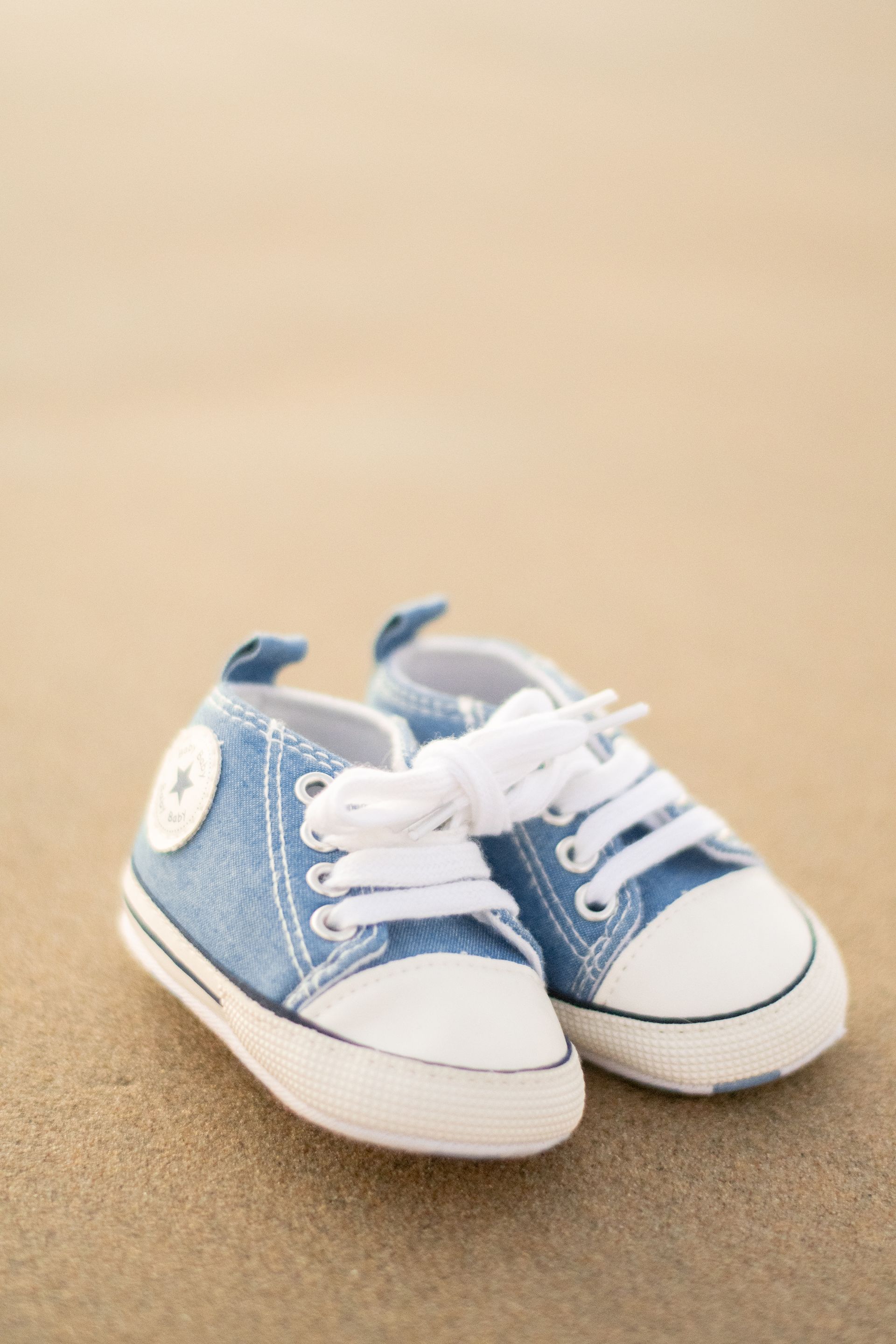 A pair of blue and white baby sneakers resting on a sandy beach.