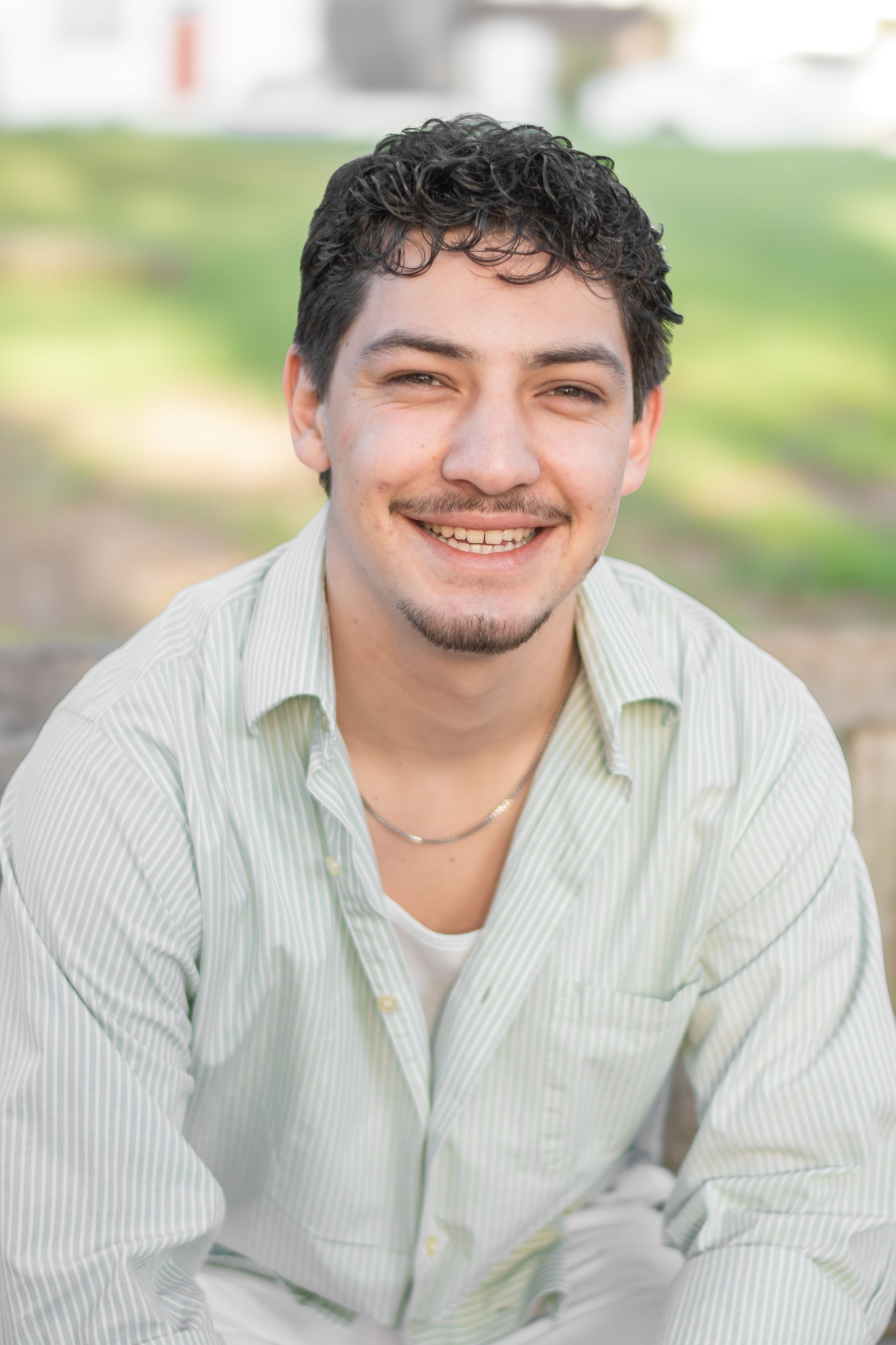 A person with curly hair and a goatee smiles in a light-colored striped shirt, set against a soft, out-of-focus background.