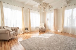An empty living room with a couch , chair , rug and chandelier.