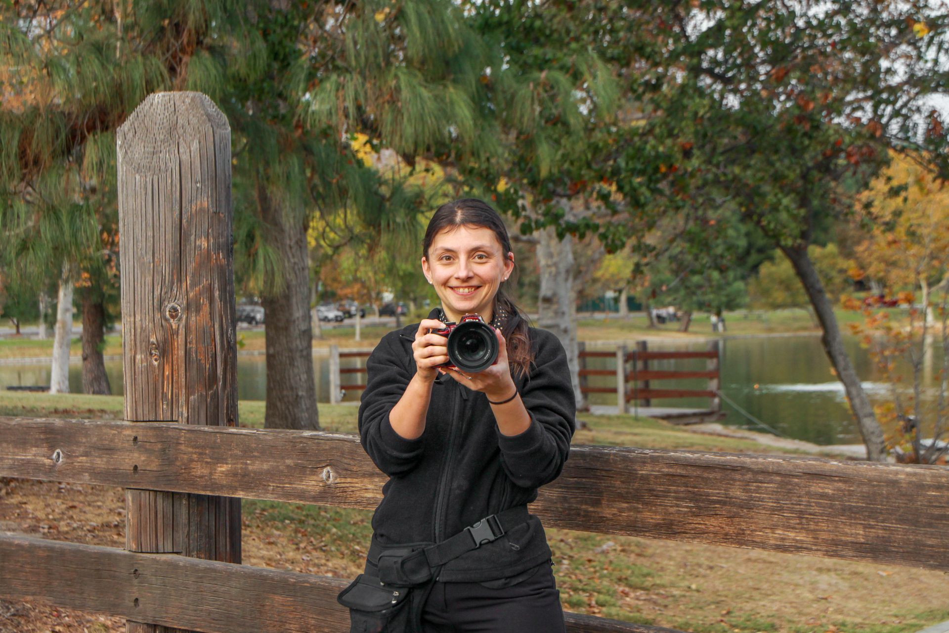 A woman is taking a picture with a camera in a park.