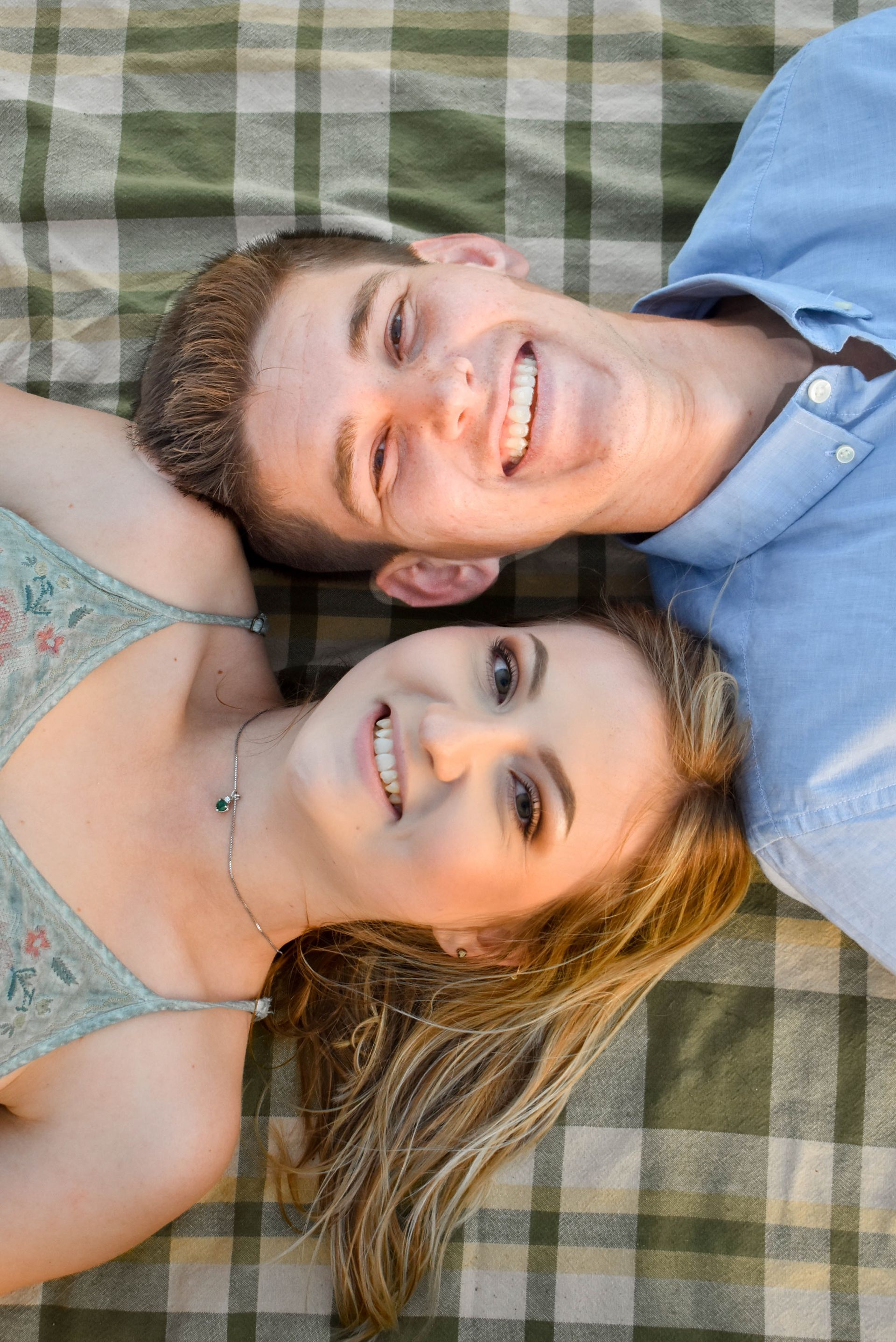 A man and a woman are laying on top of each other on a plaid blanket.