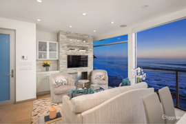 A living room with a couch , chairs , a television and a view of the ocean.