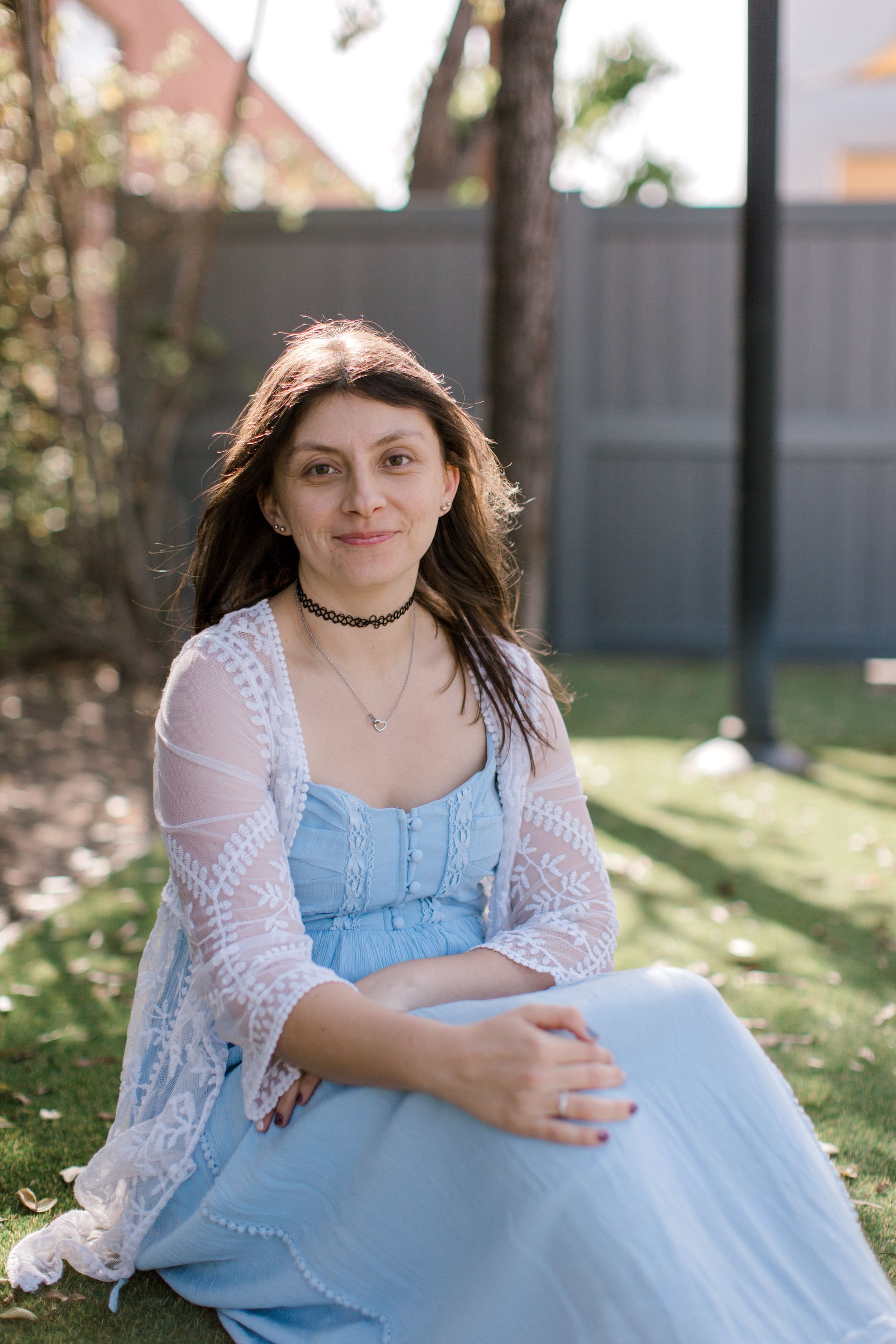 A woman in a light blue dress is sitting on the grass.