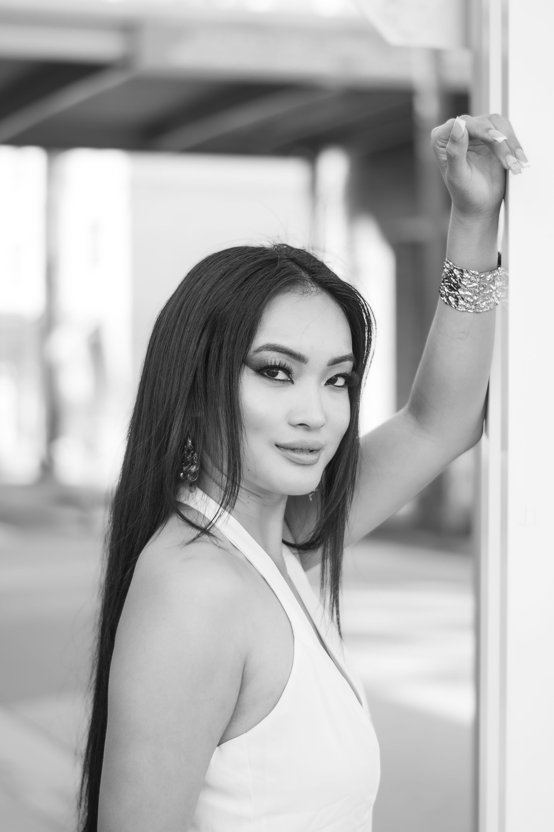 Woman posing in a white sleeveless top, looking at the camera with one arm raised outdoors