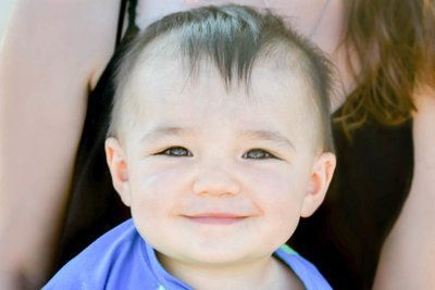 A baby is smiling for the camera while being held by a woman.
