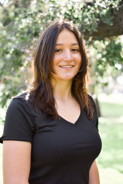 A woman in a black shirt is standing in front of a tree. Senior at Banning Park