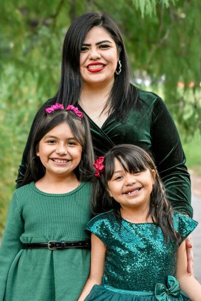 A woman is posing for a picture with two little girls in green dresses. Family. 