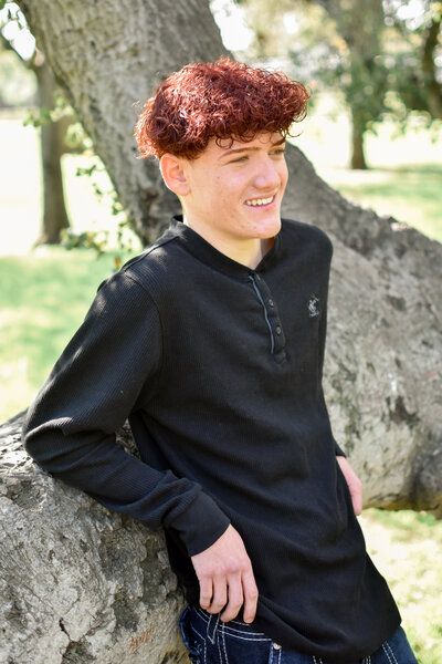 A young man with red hair is leaning against a tree in a park. Senior at Banning Park