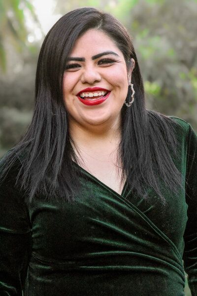 A woman in a green velvet dress is smiling for the camera.