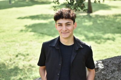 A young man in a black shirt is standing in front of a grassy field. Senior at Banning Park