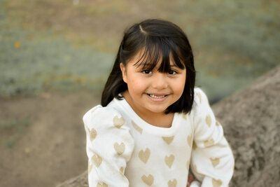 A little girl is sitting on a rock and smiling for the camera.
