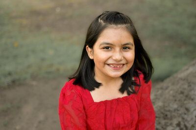 A little girl in a red dress is smiling for the camera.