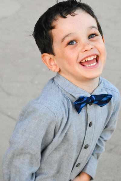 A young boy wearing a gray shirt and a blue bow tie is smiling