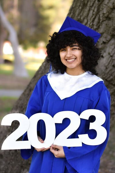 A woman in a graduation cap and gown is holding a sign that says 2023