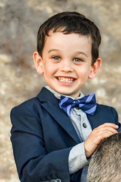 A young boy in a suit and bow tie smiles for the camera