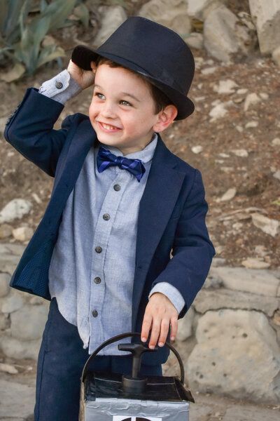 A little boy wearing a suit and hat is holding a lantern