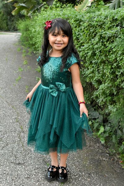 A little girl is wearing a green dress and black shoes.