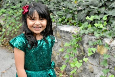 A little girl in a green dress is smiling for the camera.