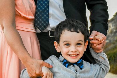 A little boy in a bow tie is being held by his parents. Family photo. 