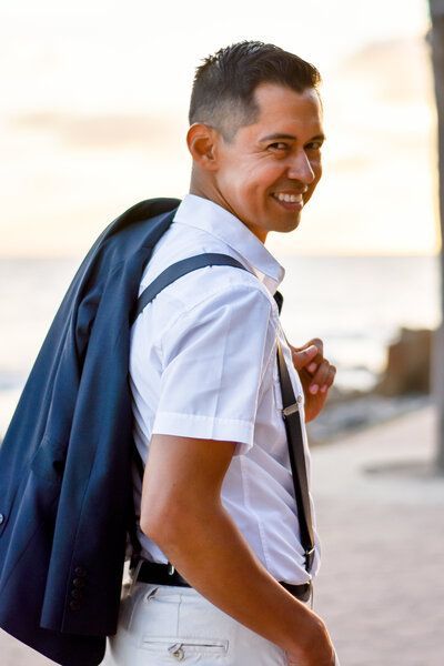 A man in a white shirt and suspenders is carrying a jacket over his shoulder.
