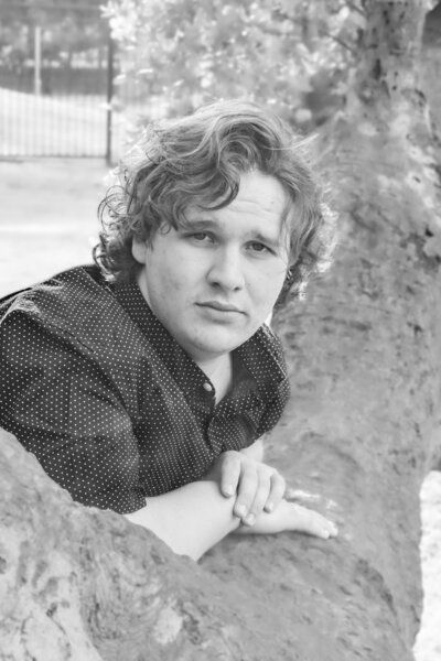 A young man leaning against a tree in a black and white photo.