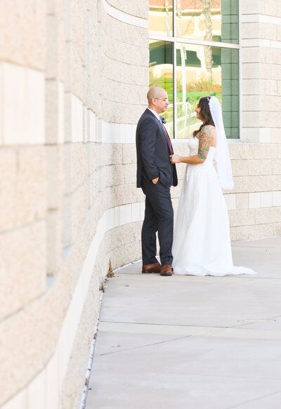 A bride and groom are standing next to each other on a sidewalk. Wedding photos