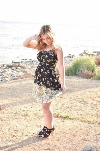 A woman in a dress is standing on a beach near the ocean.