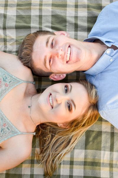 A man and a woman are laying on top of each other on a plaid blanket.
