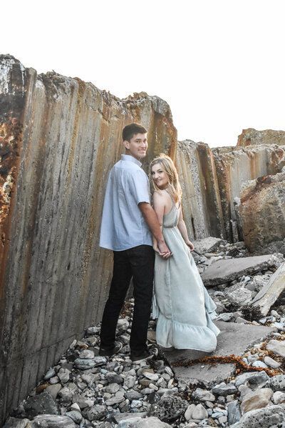 A man and a woman are standing next to each other on a rocky beach.