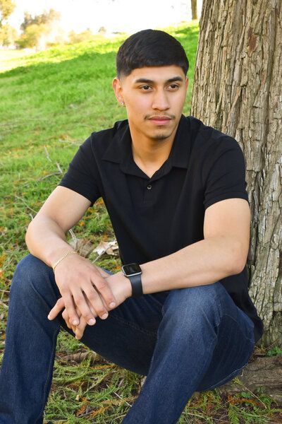 A young man in a black shirt is sitting under a tree. Senior at Averill Park. 