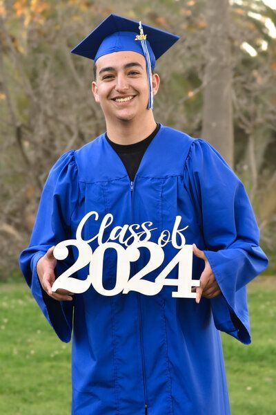 A man in a graduation cap and gown is holding a sign that says class of 2024