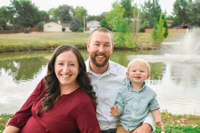 A family is posing for a picture in front of a pond.