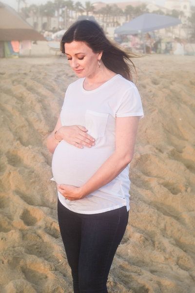 A pregnant woman is standing on a beach holding her belly. Maternity. 