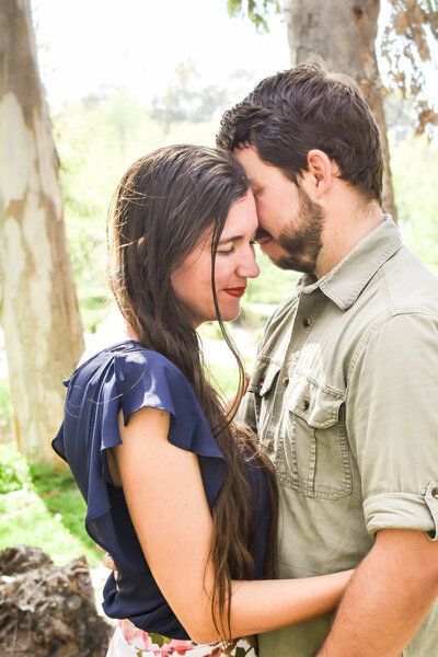 A man and a woman are standing next to each other and touching their foreheads.