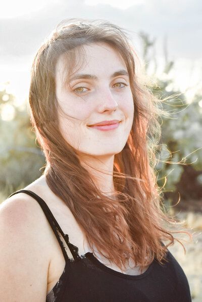 A woman with long red hair is wearing a black tank top and smiling.